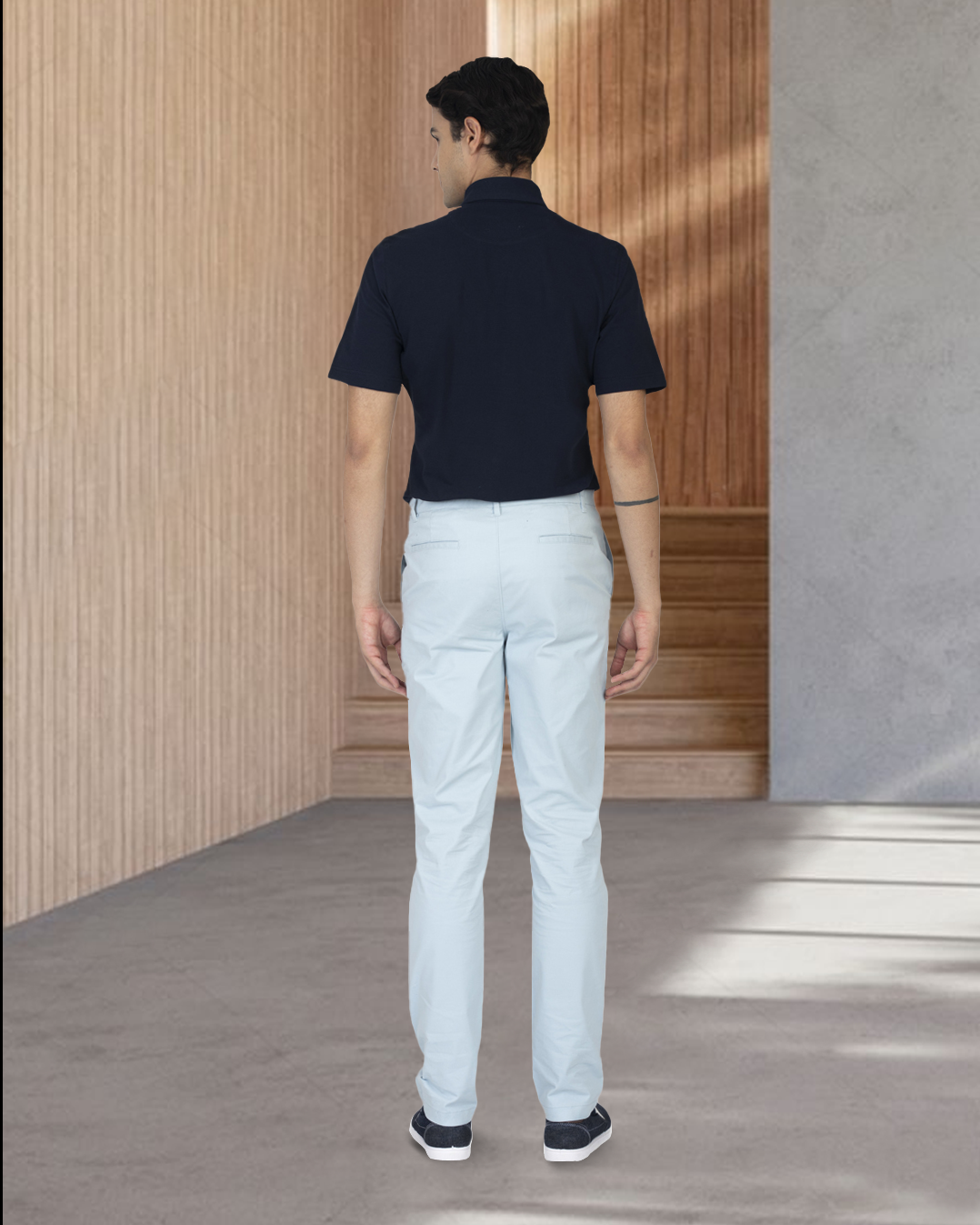Back of model wearing the custom oxford polo shirt for men by Luxire in navy with white pants