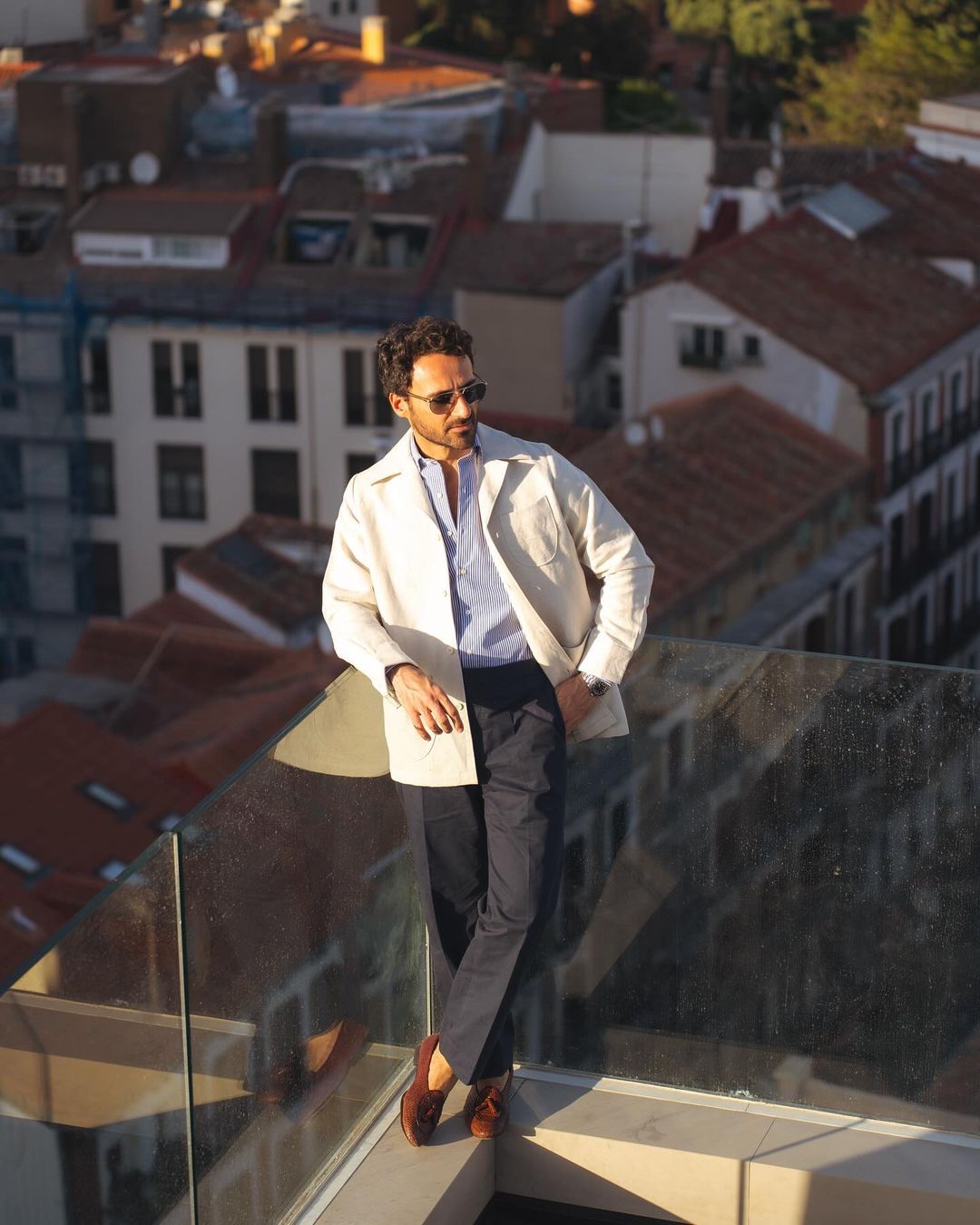 Model outside wearing the linen shirt jacket for men by Luxire in cream wearing sunglasses at top a building
